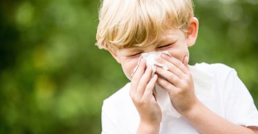 Child with seasonal allergies sneezing and holding tissue on his nose