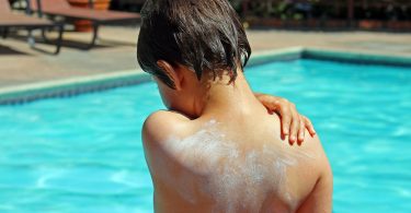 Little boy applying sunscreen by pool