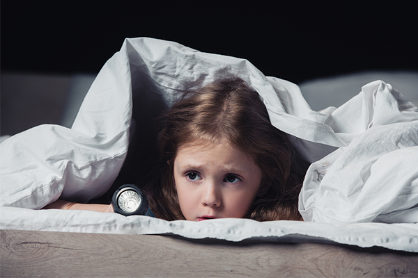 Little girl hiding under blanket with a flashlight because she is scared of the dark