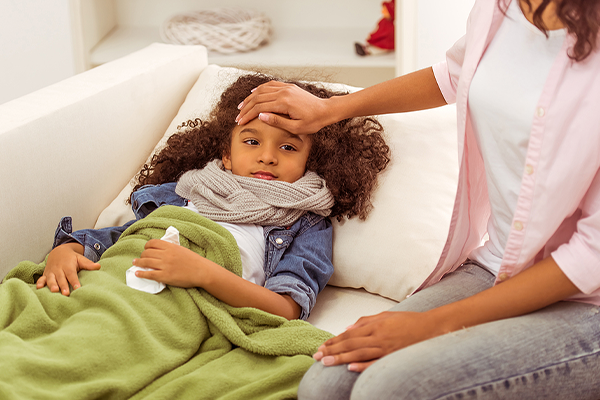 Young girl sick on sofa and mother taking temperature